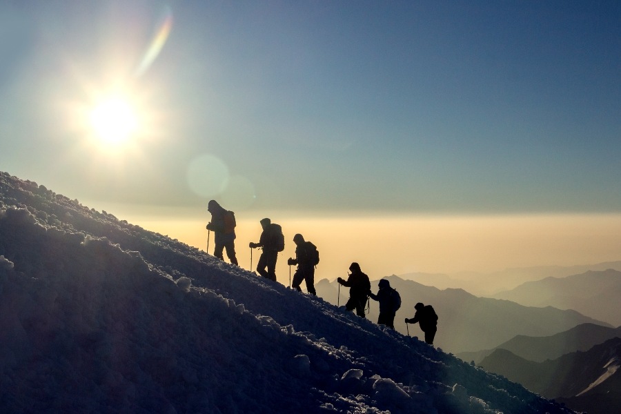 mountain climbers silhouetted by sun on side of hill